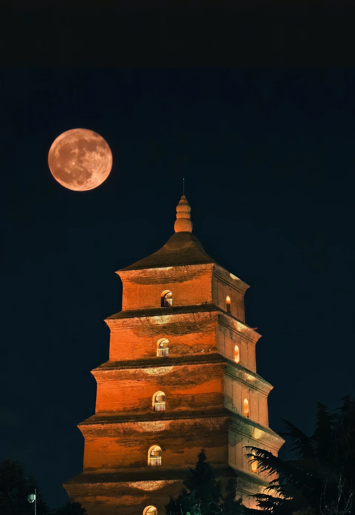 深蓝夜空与月亮下亮着暖光的古塔