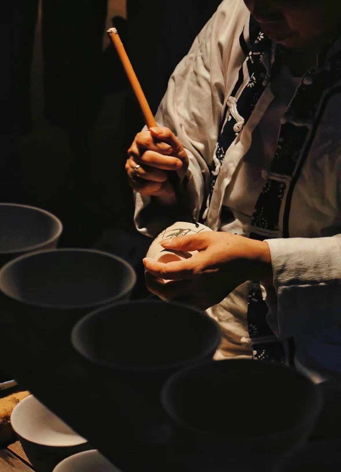 手艺人手持白色陶瓷器物,用毛笔绘制纹样